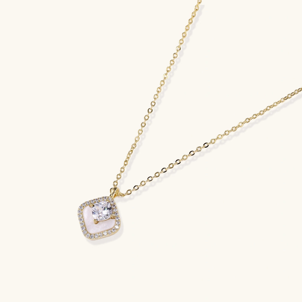 Gold quatrefoil pendant with crystal center on iridescent mother-of-pearl base, adjustable gold chain on cream background