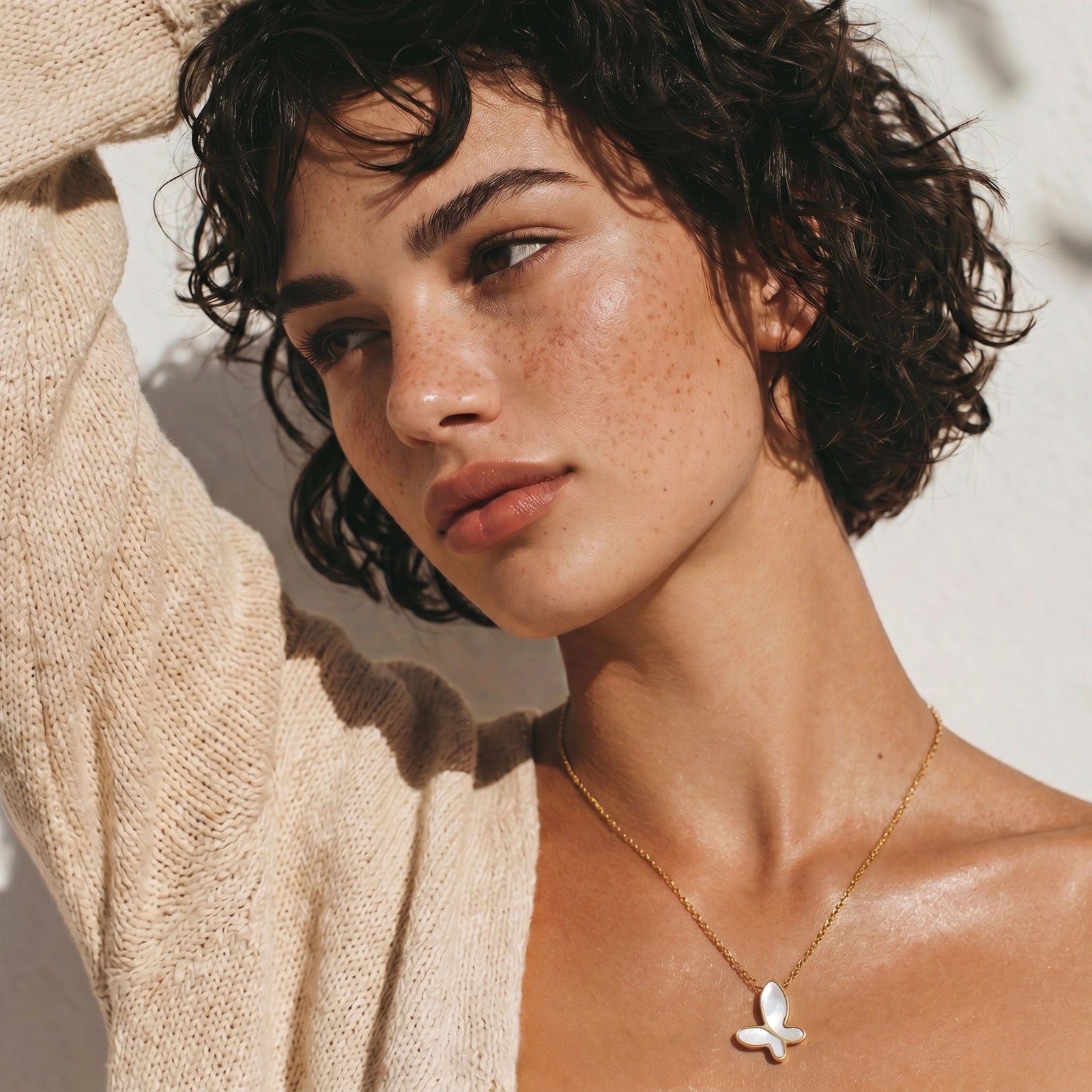 Woman wearing a gold necklace with a butterfly pendant against a neutral background